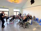 Elever i skoleorkester sidder på stole og spiller på blæseinstrumenter